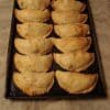 Tray of uncooked empanadas with crimped edges.