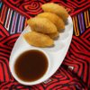 Plate of fried dumplings with dipping sauce on a colorful cloth.