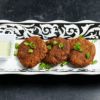 Plate of crispy fried patties garnished with green onions and a side of dipping sauce.