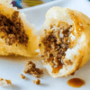 Close-up of a meat-filled steamed bun with sauce.
