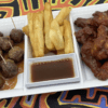 A tray with meatballs, fries, and sauced chicken wings.