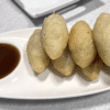 Fried dumplings served with soy dipping sauce on a white plate.