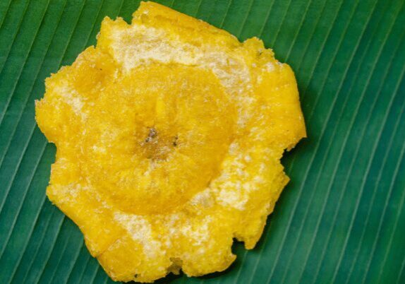 A close-up of a fried banana slice on a green leaf.