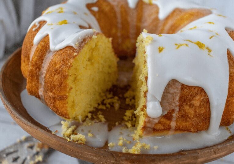 A moist bundt cake with white icing and orange zest on a plate.