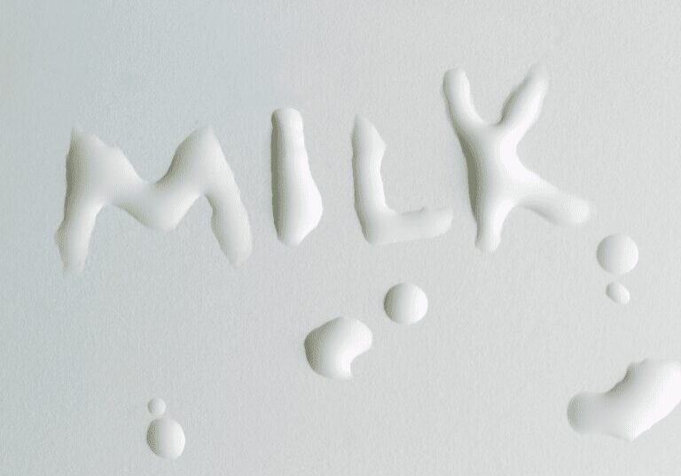 Milk spilled forming the word 'MILK' on a white surface.