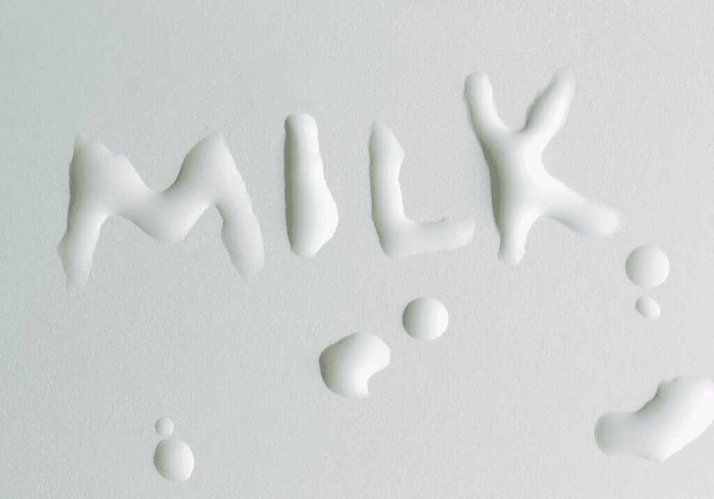 Milk spilled forming the word 'MILK' on a white surface.