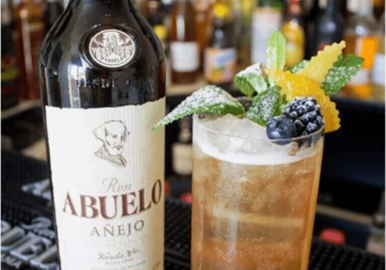 Cocktail garnished with mint, berries, and citrus, beside Abuelo Añejo rum bottle.